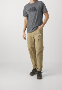 Gray short-sleeve T-shirt with black logo, paired with beige cargo pants featuring pockets and zippers, completed with dark hiking shoes.