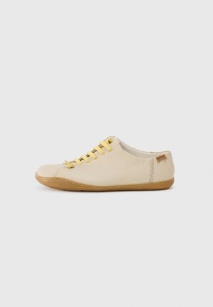 Beige leather shoe with yellow laces, round toe design, and gum sole. Slight textured finish with stitching accents and logo detail.