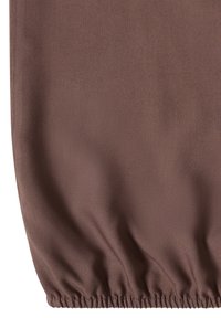 Tissu marron avec ourlet élastique froncé créant des plis doux et une forme légèrement bouffante.