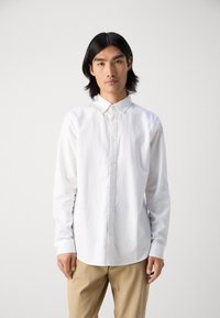 White long-sleeve button-up shirt with a collared neckline, featuring a textured fabric and subtle embroidery on the left chest.