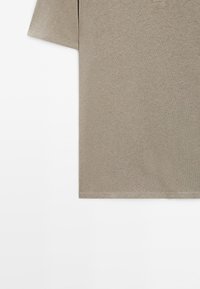 T-shirt beige à manches courtes avec une poche sur la poitrine gauche, présenté sur un fond blanc.