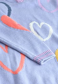 Jasnoniebieski sweter z dzianiny z dużymi, wielokolorowymi wzorami serc. Rybaczki w pastelowych odcieniach uzupełniają design. Miękka tekstura.