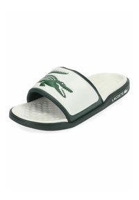 Chanclas Lacoste en blanco y verde oscuro con plantilla texturizada, logo de cocodrilo en la correa y nombre de la marca en el lateral de la suela.