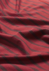 Punainen kangas tummanharmailla raidoilla, jossa on pehmeä rakenne ja hienovaraisia aaltokuvioita, aseteltuna näyttämään sen virtausta ja värieroja.