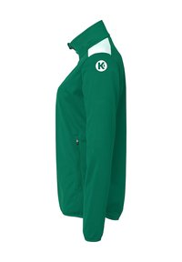 Grøn jakke med høj krave, hvide detaljer på skuldrene, lynlåslomme i siden og et cirkulært logo på ærmet. Glat stoftekstur.