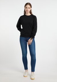 Felpa nera a maniche lunghe con maniche raglan e dettagli testurizzati ai polsini, abbinata a jeans skinny blu e sneaker bianche.