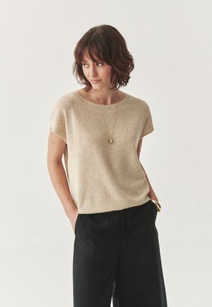 Top beige in maglia con maniche corte e scollo rotondo, abbinato a pantaloni neri a gamba larga. Texture liscia, design minimalista.