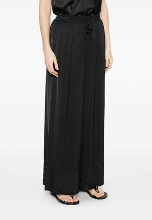 Donna che indossa una gonna nera, a gamba larga e vita alta con cintura annodata, abbinata a sandali neri bassi, su sfondo bianco.