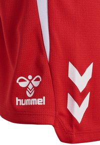 Pantaloncini sportivi rossi con logo dell'ape Hummel bianco e due chevron bianchi rivolti verso il basso su tessuto strutturato.