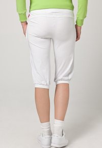 Vita cropped byxor med en avslappnad passform, elastisk nederkant och midja. Bärs med vita sneakers och en ribbad grön topp som visar upp en enkel design.