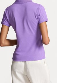 Lila piké med krage och korta ärmar, tillverkad i ett mjukt tyg, inskjuten i vita linnebyxor.