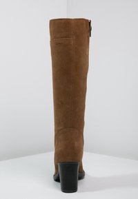 Botas de ante marrón hasta la rodilla con puntera redonda, cremallera lateral y tacón apilado negro. Textura suave con detalles de costura limpios.