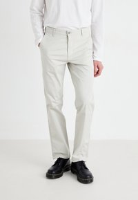 Lys grå, slim-fit bukser laget av en bomullsblandingsstoff, med glidelås og knappelukking, og sidelommer, kombinert med svarte sko.