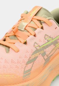 Sport shoes with a pink mesh upper, orange laces, and green accents. Features a textured surface and a cushioned sole design.