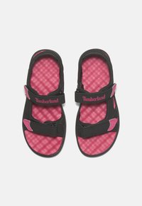Mustat sandaalit vaaleanpunaisilla yksityiskohdilla, teksturoitu pohja, säädettävät hihnat ja Timberland-merkit. Avoin varvasosa hengittävyyden vuoksi.
