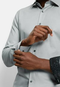 Hellgraues Hemd aus strukturierter Baumwolle, mit Button-Down-Kragen und dunkelgrauen gemusterten Manschetten. Verfügt über passende Knöpfe und eine schmale Passform.