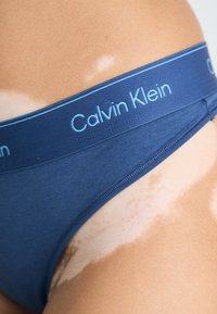 Culotte de bikini en coton navy avec un logo Calvin Klein bleu clair sur la taille. Texture douce et bords sans coutures.