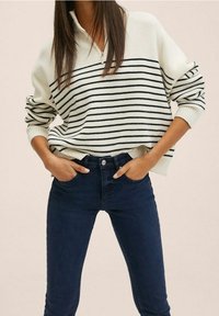 Bílý pletený svetr s černými horizontálními pruhy, s polozipem. V kombinaci s tmavě modrými skinny džínami. Texturovaná tkanina.