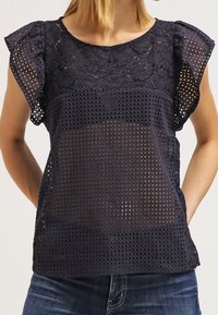 Haut bleu marine à manches courtes volantées, avec des détails en dentelle et un motif perforé. Tissu doux avec une apparence texturée.