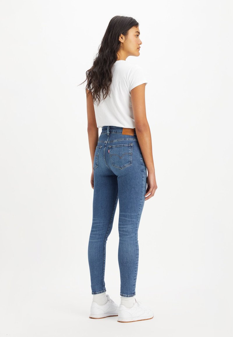 Jeans en denim bleu taille haute avec une coupe fuselée, dotés de poches arrière, d'un patch en cuir et d'un léger stretch pour plus de confort.