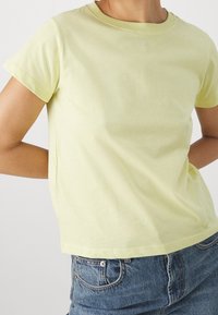 Ljusgul t-shirt med kort ärm gjord av mjuk bomull. Rundad halsringning, avslappnad passform, med minimalistisk design utan synliga mönster.