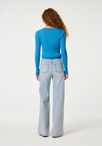 Blauwe geribde longsleeve top gecombineerd met lichtblauwe wijde jeans. Opmerkelijke details zijn de textuur van de stof van de top en het logo op de achterkant.