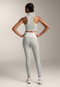 Világosszürke sportos crop top és magas derékú leggings sárga kiegészítőkkel, sima, rugalmas anyagból készült. Sportos dizájn, testhezálló forma.