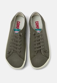 Sneakers verdi in tela con suole in gomma bianca, dotati di sei occhielli, lacci coordinati e un logo rosso sulle sole.
