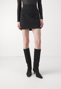 Mustat mini-hameet, joissa on tyylikäs muotoilu ja korkea vyötärö, hienovaraiset saumat, yhdistettynä polven ylle ulottuviin mustiin korkokenkiin, sileä pinta.