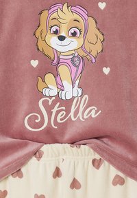 Girls' pajama set featuring a pink top with a cartoon dog and the name "Stella," paired with cream bottoms decorated with pink hearts.
