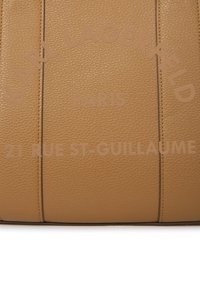 Nærbilde av beige teksturert skinn med "KARL LAGERFELD PARIS 21 RUE ST-GUILLAUME" preget i matchende farge.