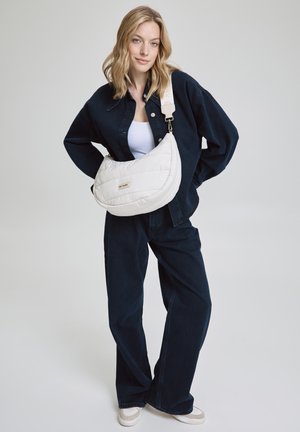 Weiße gesteppte Schultertasche mit geschwungener Form, silbernem Hardware und verstellbarem Riemen, kombiniert mit einem navyfarbigen Denim-Outfit.