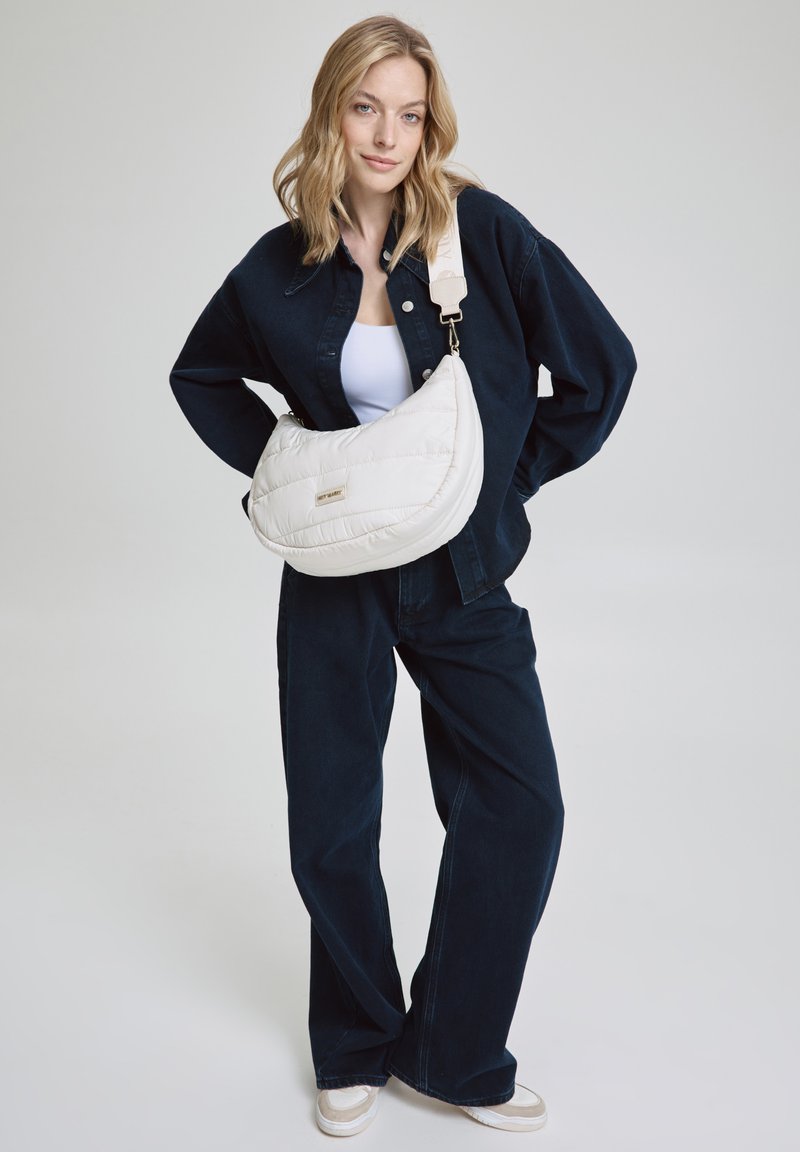 Sac en bandoulière blanc matelassé de forme courbée, avec quincaillerie argentée et bandoulière réglable, associé à une tenue en denim bleu marine.