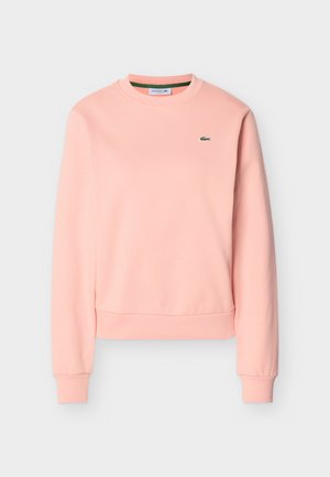 Duga ružičasta majica dugih rukava s okruglim izrezom, s rebrastim manžetnama i rubom, s malim zelenim logom krokodila Lacoste na prsima.