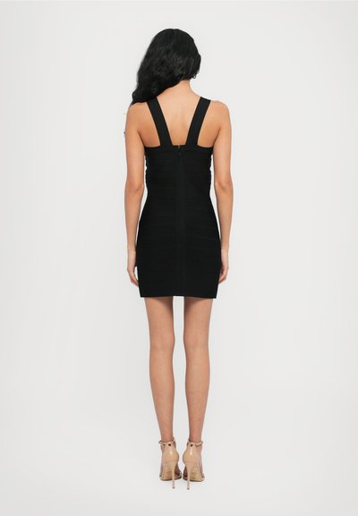 Rochie neagră din material elastic, cu o siluetă ajustată, bretele largi și fermoar la spate. Textură netedă și tăiere până la genunchi. Tocuri transparente înalte vizibile.