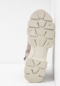 Chaussure en suede gris clair avec une semelle en caoutchouc blanc texturé présentant un motif en zigzag, des formes carrées et des nervures pour une meilleure adhérence.