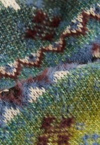 Couverture en tricot présentant une palette de couleurs verte, bleue et jaune, avec une surface texturée et des motifs en zigzag et en étoile marron.
