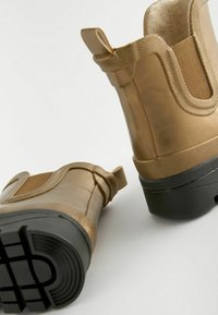 Stivali ankle waterproof dorati con suole in gomma, finitura texturizzata, pannelli laterali elasticizzati e linguette per una facile calzata.