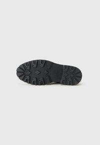 Suela de calzado de goma negra con un diseño robusto, que presenta surcos profundos y patrones geométricos para proporcionar tracción y estabilidad.