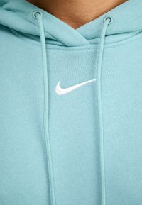Haut à capuche bleu clair en matériau doux. Présente un logo Nike brodé blanc sur la poitrine et un cordon de serrage pour un ajustement.