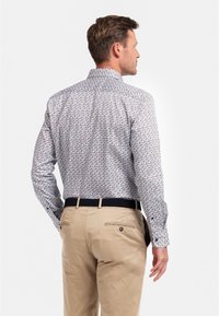 Herenoverhemd, lichte stof, multikleurig geometrisch patroon, lange mouwen, knoopsluiting kraag, gecombineerd met beige broeken en een zwarte riem.