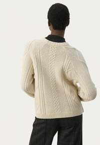 Kabelstrikket sweater i creme med teksturerede mønstre, ribbede manchetter og kant, samt en rund hals. Har raglanærmer og en varm konstruktion.