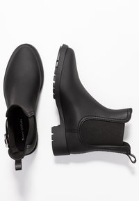 Bottines en caoutchouc noir avec des panneaux latéraux élastiques, des semelles texturées et des languettes pour un enfilage facile. Fini lisse dans l'ensemble avec des détails subtils.