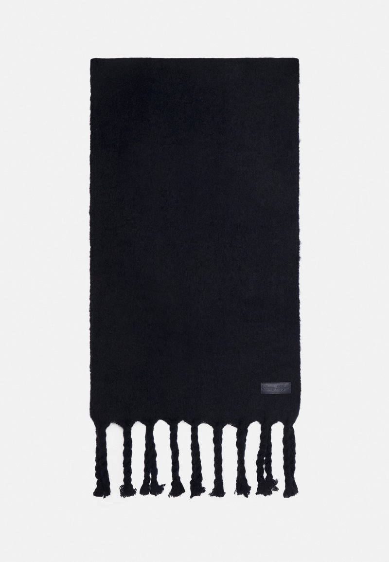 Écharpe noire tissée avec des franges torsadées en bas. Texture douce et forme rectangulaire, avec une petite étiquette en cuir sur un bord.