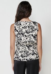 Top senza maniche in crema chiaro con motivo floreale nero. Vita elastica, tessuto morbido e scollatura rotonda, che offrono una silhouette aderente.