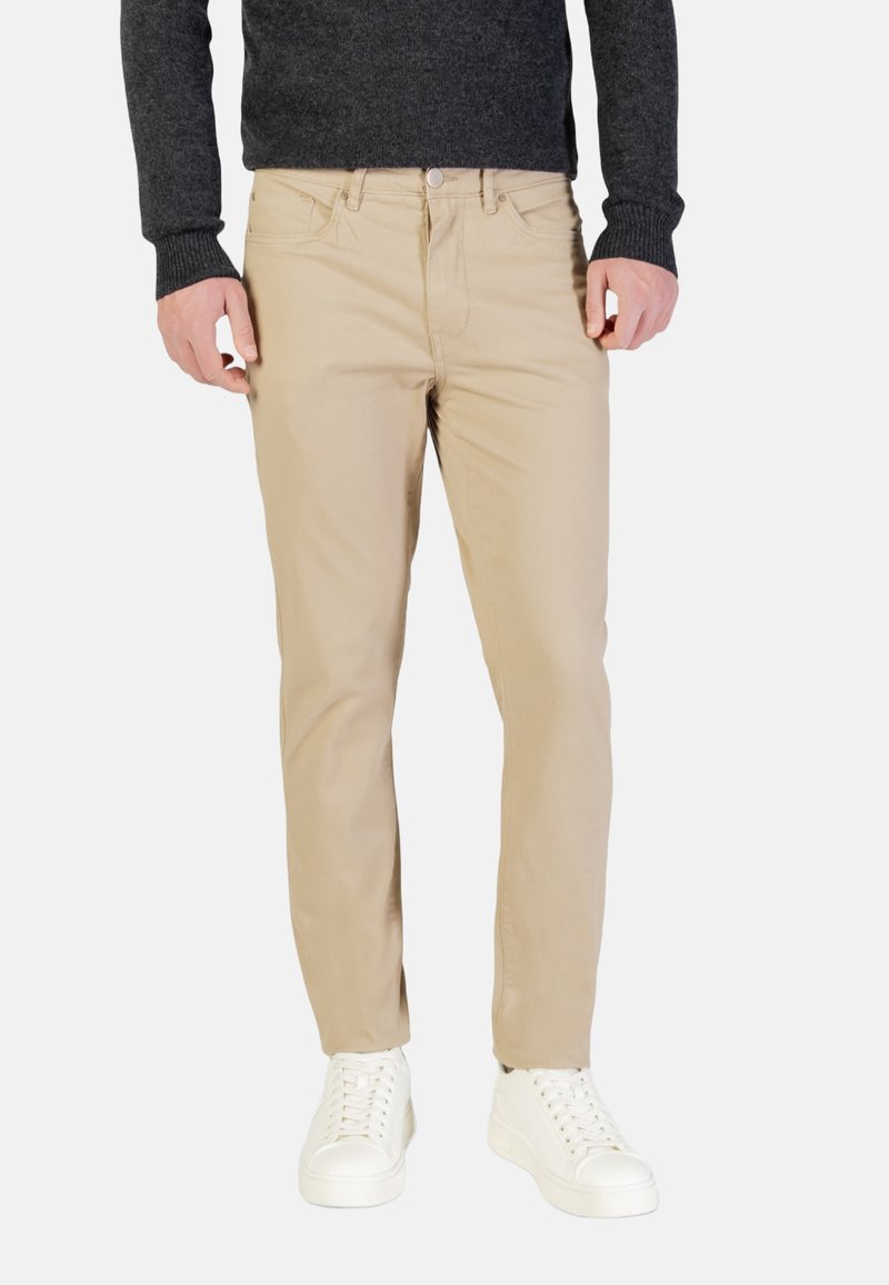 Chinos beige de algodón con corte recto, con diseño de cinco bolsillos y cierre de cremallera. Combinados con zapatillas blancas y un suéter gris oscuro.