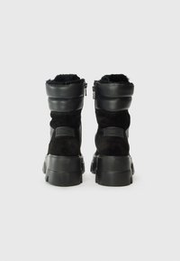 Bottines noires avec doublure en fausse fourrure, présentant une tige en cuir lisse, une semelle épaisse et une fermeture éclair sur le côté pour un enfilage facile.