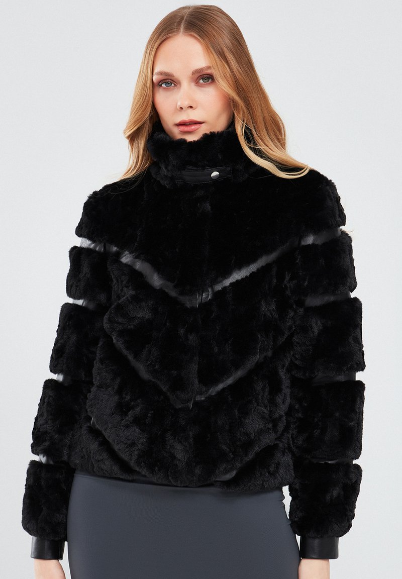Black faux fur jacket with chevron panel design and high collar. Features smooth, sleek accents on sleeves and a sturdy zipper closure.
