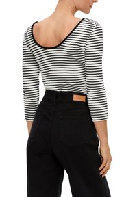 Schwarz-weißer gestreifter Langarmshirt mit weitem Rundhalsausschnitt, tailliert und kombiniert mit hochgeschnittenen schwarzen Jeans mit Gesäßtaschen.