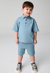 Ljusblå pikétröja med krage och tre mörka knappar, matchad med shorts i samma färg. Svarta höga sneakers fulländar outfiten.